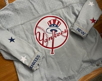 May include: Light blue denim jacket with a large Yankees logo on the back. The logo is red, white, and blue. The jacket has star accents on the sleeves and small rhinestones. The sleeves say "NEW" and "YANKEES".