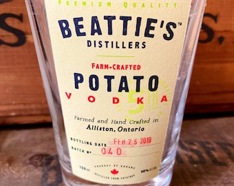 May include: A clear glass bottle of Beattie's Farm-Crafted Potato Vodka. The label is yellow with black text and red accents. The bottle is 750 ml and 40% alcohol by volume. The bottling date is February 26, 2019, and the batch number is 040.