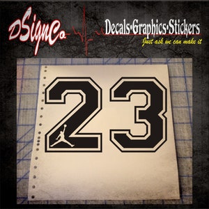 May include: Black and white number 23 with a basketball player silhouette inside the number 2. The numbers are in a bold, blocky font.