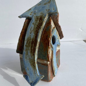 May include: A blue and brown ceramic birdhouse with a unique arrow design. The birdhouse has a small opening for birds to enter.