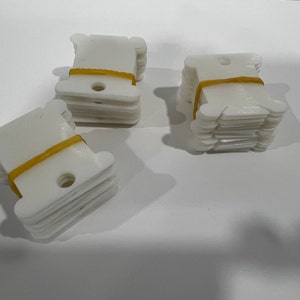 May include: Three stacks of white plastic thread bobbins, each stack secured with a yellow rubber band.