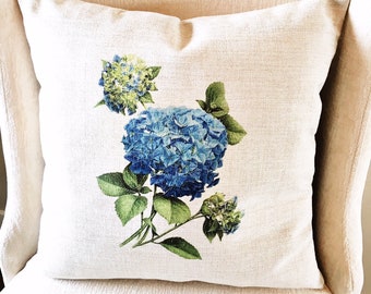 May include: A white pillow with a blue and green hydrangea floral print. The pillow is on a white chair.
