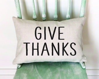 May include: A light green wooden chair with a beige pillow that says "GIVE THANKS" in black lettering.