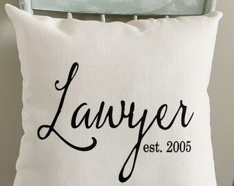 May include: White throw pillow with black cursive text that reads "Lawyer est. 2005".