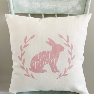 May include: A white pillow with a pink bunny silhouette and the text "hello spring" in a pink wreath.