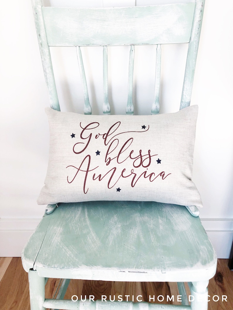 May include: A white pillow with the text "God Bless America" in red cursive lettering and blue stars. The pillow is sitting on a light green painted chair.