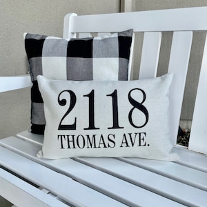 May include: White bench with two pillows. The top pillow is white with black text that reads "2118 Thomas Ave.". The bottom pillow is black and white buffalo plaid.