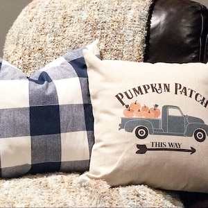 May include: A throw pillow with a white background and a blue truck carrying pumpkins. The text "Pumpkin Patch This Way" is printed on the pillow.
