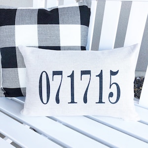 May include: A white bench with two pillows. The top pillow is black and white buffalo plaid. The bottom pillow is white with the number 071715 printed in black.