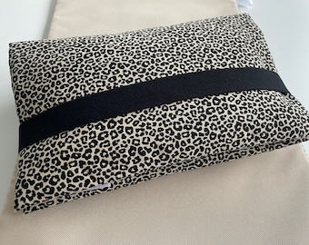 May include: A beige and black leopard print pillow with a black elastic band across the middle.