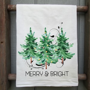Peut inclure: Serviette de cuisine blanche avec une illustration aquarelle de trois sapins de No&euml;l verts avec des ornements color&eacute;s et le texte "Merry & Bright".