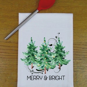 Peut inclure: Serviette de cuisine blanche avec une illustration aquarelle de trois sapins de No&euml;l verts avec des ornements color&eacute;s et le texte "Merry & Bright".