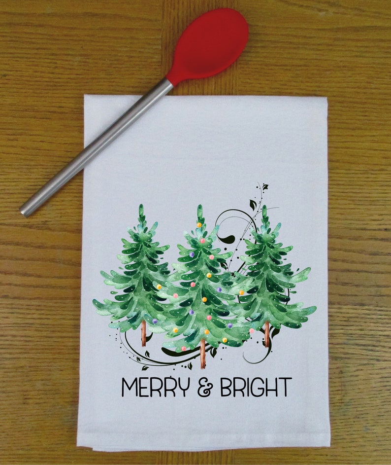 Peut inclure: Serviette de cuisine blanche avec une illustration aquarelle de trois sapins de No&euml;l verts avec des ornements color&eacute;s et le texte "Merry & Bright".