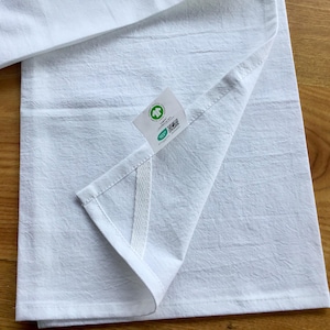 Peut inclure: Une serviette de cuisine blanche avec une &eacute;tiquette verte et blanche indiquant "Compostable & Biod&eacute;gradable" et un code QR. La serviette a une couture blanche sur le c&ocirc;t&eacute;.