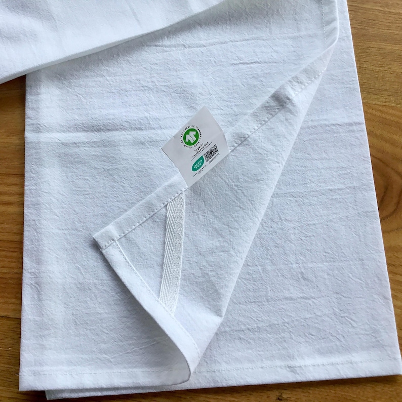 Peut inclure: Une serviette de cuisine blanche avec une &eacute;tiquette verte et blanche indiquant "Compostable & Biod&eacute;gradable" et un code QR. La serviette a une couture blanche sur le c&ocirc;t&eacute;.