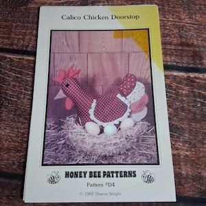 May include: A sewing pattern booklet titled Calico Chicken Doorstop by Honey Bee Patterns, Pattern #D4, 1982 Sharon Wright. The cover features a photograph of a fabric chicken with red polka dots, a white lace apron, and three eggs in a nest.