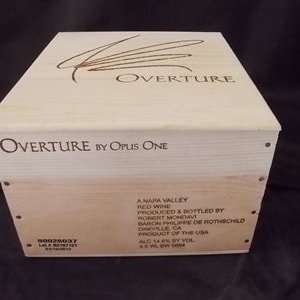 May include: A light-colored wooden wine box with the word "OVERTURE" and a stylized design on the lid. The box is labeled "OVERTURE BY OPUS ONE" and includes text indicating it contains Napa Valley red wine.