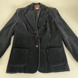 Peut inclure: Un blazer en velours gris anthracite foncé doté d'un revers cranté, de manches longues et de deux poches plaquées à l'avant. La veste se ferme avec deux boutons rouge foncé sur le devant et possède une doublure intérieure avec une étiquette.