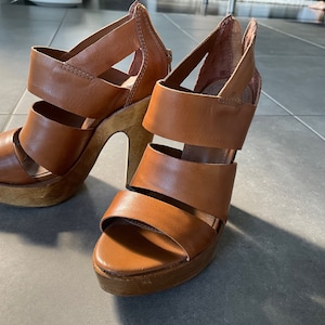 May include: A pair of brown leather heeled sandals with multiple straps. The sandals have a wooden platform and a high heel.