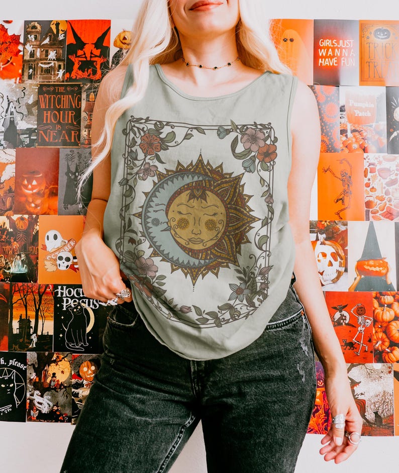 Op de afbeelding: Een lichtgroene tanktop met een zon- en maanontwerp met bloemaccenten. De afbeelding is omlijst door een decoratieve rand. De tanktop wordt gecombineerd met een zwarte jeans. De achtergrond bevat Halloween-thema posters.