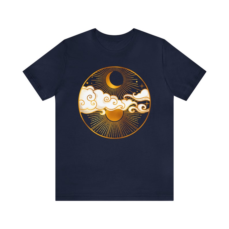 K&ouml;nnte beinhalten: Ein marineblaues T-Shirt mit einem goldenen kreisf&ouml;rmigen Design, das eine Mondsichel, die Sonne und Wolken zeigt. Das Design erinnert an eine himmlische Szene.