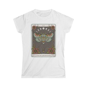May include: White t-shirt with a graphic of a tarot card featuring a moth with floral accents and the text "XVII THE METAMORPHOSIS".
