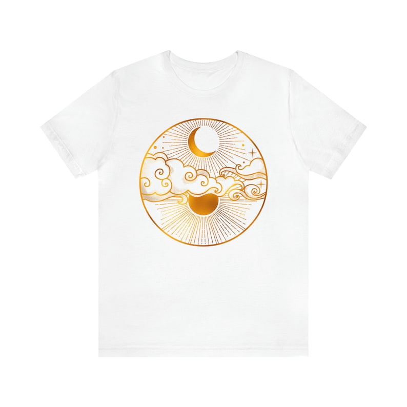 K&ouml;nnte beinhalten: Wei&szlig;es T-Shirt mit einem goldenen Motiv einer Sonne und eines Mondes mit Wolken und Sternen.