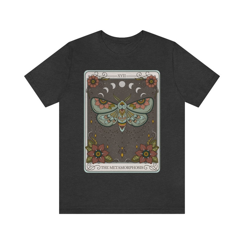 May include: A dark grey t-shirt with a graphic of a tarot card featuring a moth with floral accents and the text "XVII THE METAMORPHOSIS".