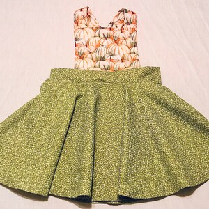 May include: A green and white patterned skirt with a pumpkin print bodice. The skirt is a-line and has a gathered waist.