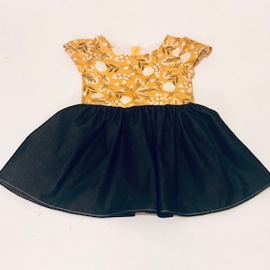 May include: A yellow and white floral print dress with a black denim skirt. The dress has short sleeves and a round neckline.