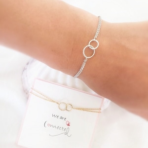 May include: Two delicate silver and gold chain bracelets with interlocking circle charms. The bracelets are displayed on a white card with the text "We are connected" and a small pink heart.