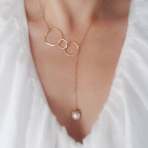 May include: A gold chain necklace with three interconnected circles and a single pearl pendant.