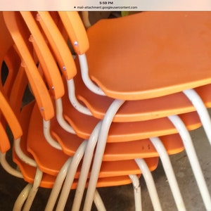 May include: A stack of six orange plastic chairs with white metal legs. The chairs are stacked in a staggered pattern, with the legs of the top chair visible.