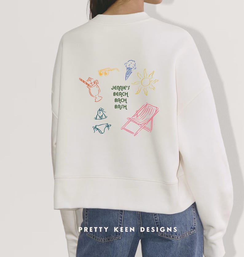May include: White sweatshirt with colorful beach-themed graphics, including a sun, ice cream cone, and beach chair. The text "Jennie's Beach Bash" is also featured. The bottom of the sweatshirt has the text "Pretty Keen Designs".