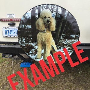 May include: A spare tire cover with a white standard poodle in a snowy forest setting. The cover is black with a white border. The text "EXAMPLE" is superimposed over the image in red.