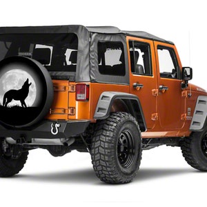 May include: A black spare tire cover with a silhouette of a wolf howling at the moon. The cover is on a orange Jeep Wrangler.