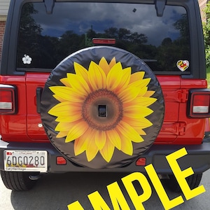 May include: A red Jeep Wrangler with a black spare tire cover featuring a yellow sunflower design. The license plate reads "6DG0280".