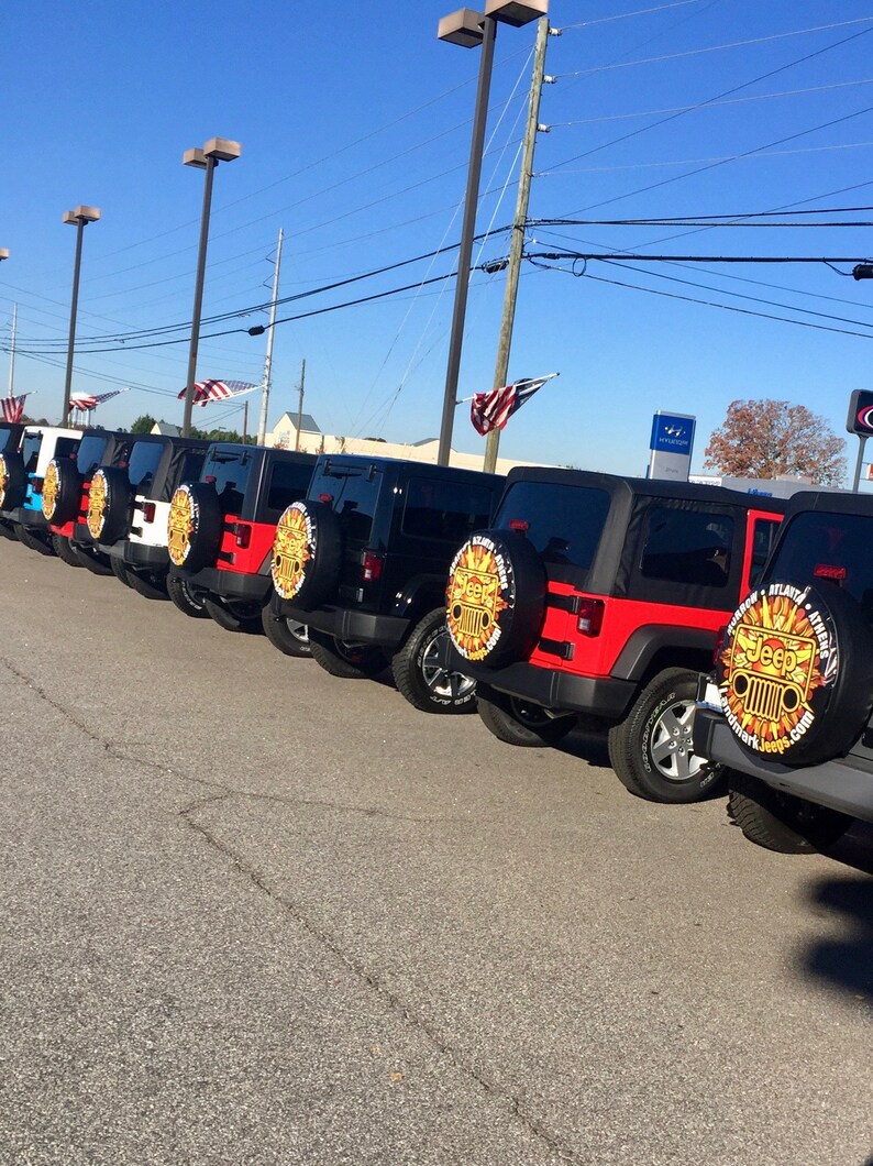 May include: A row of black and red Jeep Wranglers with custom gold and black spare tire covers. The spare tire covers have the Jeep logo and the words "Atlanta Jeep" and "Jeepmark.com".