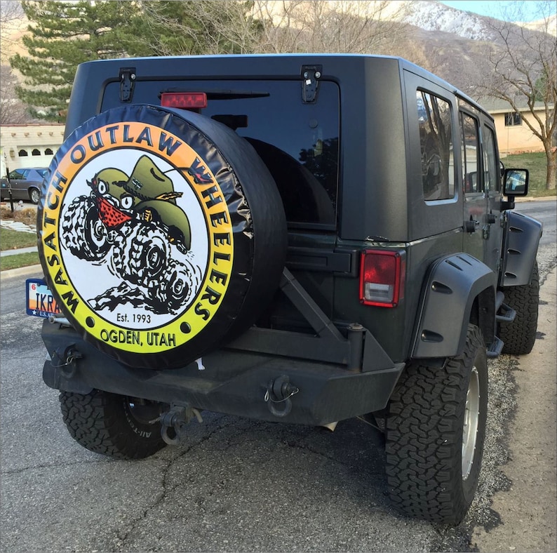 May include: A black Jeep Wrangler with a spare tire cover that says "Wasatch Outlaw Wheelers Est. 1993 Ogden, Utah".