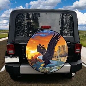 May include: A black Jeep with a spare tire cover featuring a bald eagle flying over a desert landscape with a sunset in the background.