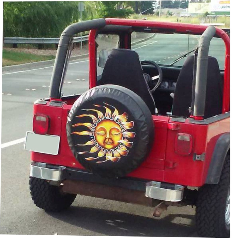 May include: A red Jeep with a black spare tire cover featuring a yellow sun with a closed-eye face and yellow rays.