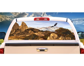 May include: A truck's rear window with a decal of a mountain landscape and a bald eagle flying overhead. The decal is printed in shades of brown, green, and blue.