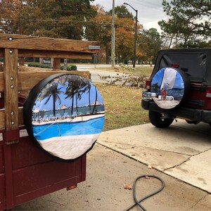 May include: Two spare tyres with custom covers. One cover features a tropical beach scene with a swimming pool and palm trees. The other cover features a sailboat and two people on a beach.