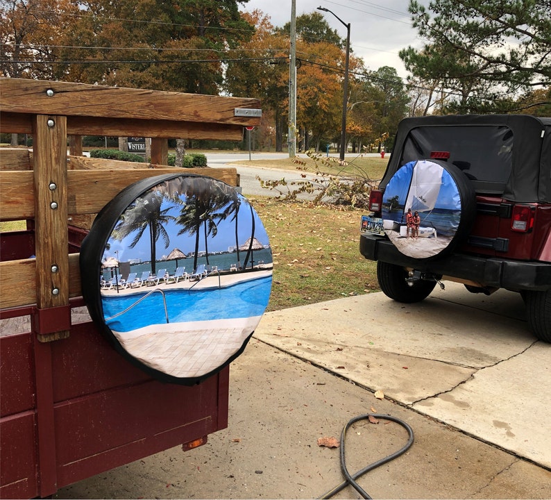 May include: Two spare tyres with custom covers. One cover features a tropical beach scene with a swimming pool and palm trees. The other cover features a sailboat and two people on a beach.