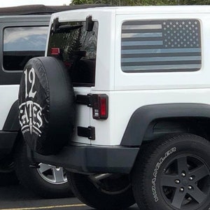 May include: White Jeep Wrangler with a black spare tire and a black American flag decal on the rear window. The spare tire has a black and white logo that says "12 Gates Brewing Company".
