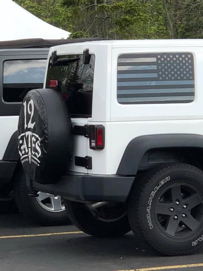 May include: White Jeep Wrangler with a black spare tire and a black American flag decal on the rear window. The spare tire has a black and white logo that says "12 Gates Brewing Company".