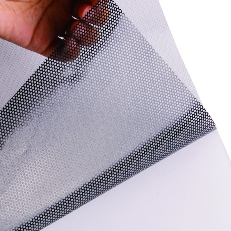 May include: A sheet of black and white perforated vinyl with a grid pattern. The vinyl is being peeled back to reveal the adhesive backing.