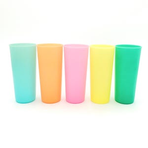 May include: Five colorful plastic tumblers in a row. The tumblers are in shades of teal, orange, pink, yellow, and green. The cups are cylindrical and have a smooth, matte finish. The background is plain white.