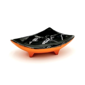 May include: A black ceramic dish with an orange rim and three legs. The dish is shaped like a boat and has a glossy finish.