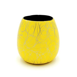 May include: A yellow ceramic vase with a black rim and a silver swirl design.